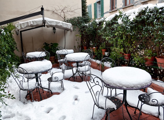 Ogród zimą ze stołami i krzesłami z kutego żelaza pokryty głębokim śniegiem.