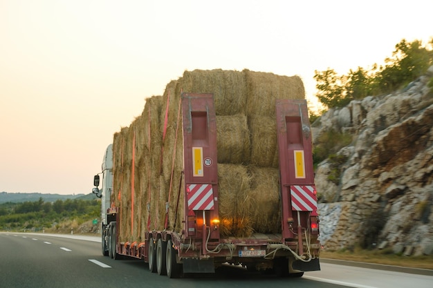 Ogromna ciężarówka transportuje bele siana w świetle zachodzącego słońca