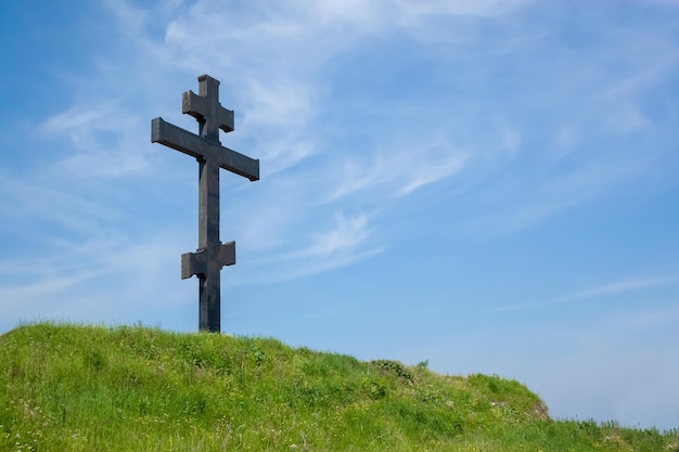 Ogromny metalowy ciemnoszary krzyż na górze na tle błękitnego nieba Letni dzień Koncepcja wiary i nadziei
