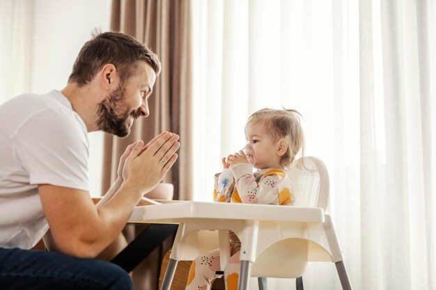 Ojciec animuje swoją chorą córkę, która siedzi na krześle i wdycha nebulizator