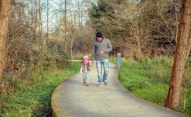 Ojciec i córka spacerują razem, trzymając się za ręce nad drewnianą ścieżką do lasu