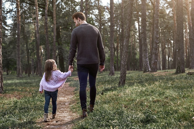 Ojciec i córka spacerują razem w lesie, jesienny dzień. Mała dziewczynka i jej tata odkrywania przyrody na zewnątrz. Kolorowe jesienne liście. Widok z tyłu