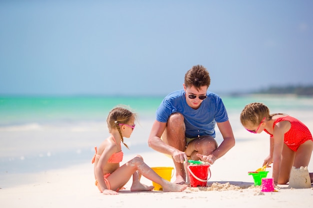 Ojciec i dzieci co zamek z piasku na tropikalnej plaży. Rodzina bawi się zabawkami na plaży