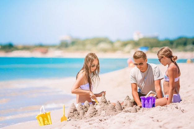 Ojciec i dzieci co zamek z piasku na tropikalnej plaży. Rodzina bawić się zabawkami plażowymi