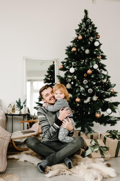 Ojciec i małe dziecko bawią się i bawią razem w domu Portret kochającej rodziny z bliska Wesoły tata przytula uroczą córeczkę w pobliżu choinki Wesołych Świąt i Wesołych Świąt