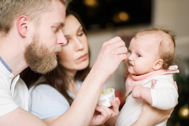 Ojciec i mama karmią swoje dziecko puree owocowym w kuchni łyżką