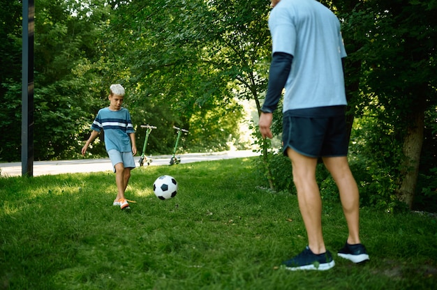 Ojciec i syn grają w piłkę nożną na trawie na świeżym powietrzu. Rodzina prowadzi zdrowy tryb życia, poranny trening fitness w letnim parku