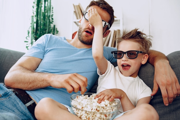 Ojciec i syn oglądają filmy w domu w okularach 3d i jedzą popcorn