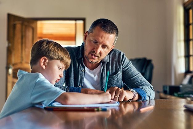 Ojciec i syn pomagają z zadaniami domowymi w edukacji, wspierają i dbają o naukę i wzrost przedszkolny Mężczyzna i chłopiec w domu z pisaniem w książce dla języka, matematyki i umiejętności dla rozwoju dziecka