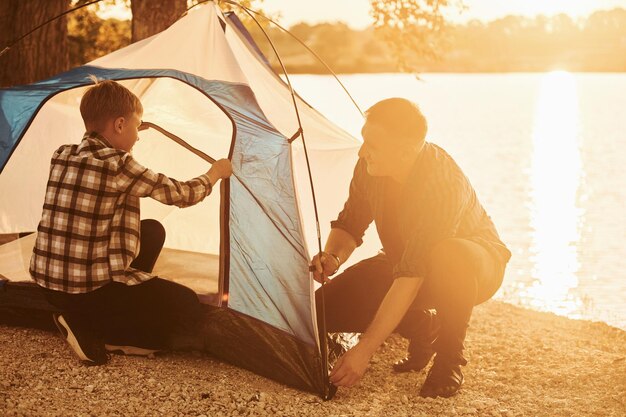 Ojciec i syn rozbijają namiot na zewnątrz w pobliżu jeziora