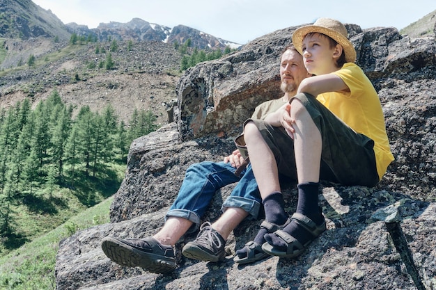 Ojciec i syn siedzą na kamieniu wysoko w górach i podziwiają piękną przyrodę Spokój i jedność z naturą