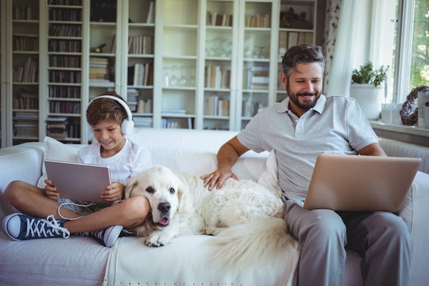 Ojciec i syn siedzi na kanapie i przy użyciu cyfrowego tabletu i laptopa