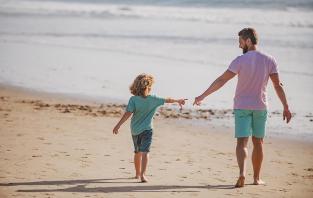 Ojciec i syn spacerują po letniej plaży Tata i dziecko trzymają się za ręce i idą razem