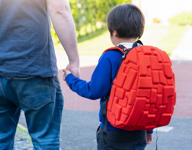 Ojciec i syn trzymając się za ręce razem, uczniak przewożący plecak spaceru do szkoły