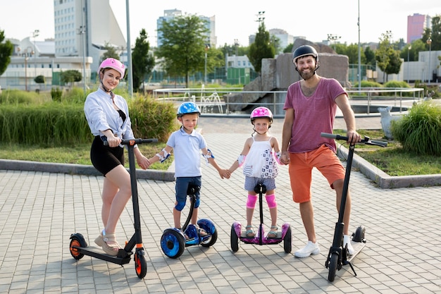 Ojciec, matka, córka i syn w kaskach stoją w parku na skuterach elektrycznych. Aktywny styl życia.