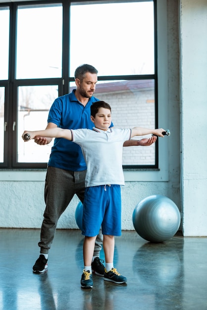 Ojciec pomaga synowi ćwiczyć z hantlami na siłowni