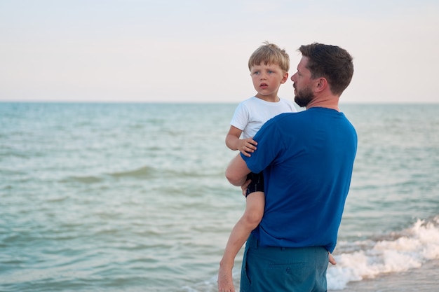 Ojciec syn spędzać czas razem wakacje na morzu Młody tata dziecko mały chłopiec spaceru plaży Dzień Ojca. Rodzina z jednym dzieckiem. Szczęśliwe dzieciństwo z tatą. śmieje się siedząc na rękach