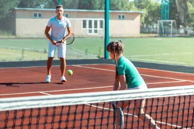 Ojciec ubrany w białą odzież sportową, grający w tenisa ze swoim dzieckiem