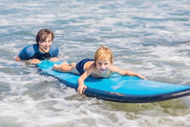 Ojciec uczy swojego młodego syna, jak surfować po morzu na wakacjach lub wakacjach. Koncepcja podróży i sportu z dziećmi