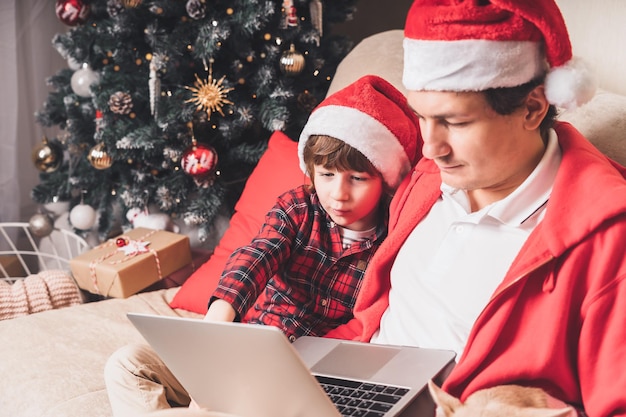 Ojciec z dzieckiem dziecko syn i pies szczeniak w santa hat na święta Bożego Narodzenia siedzi na kanapie mając