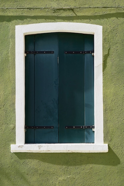 Zdjęcie okno z zielonymi okiennicami na zielonej ścianie domów. włochy, wenecja, burano.