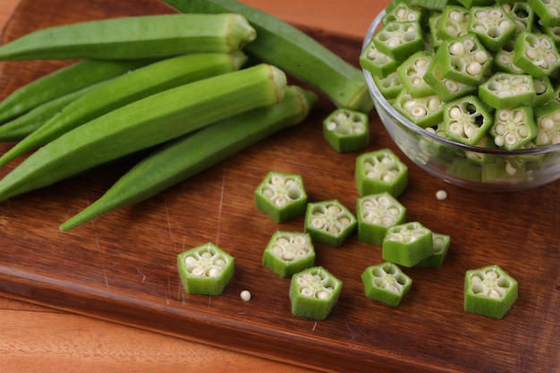 Okra lub palec Ladys lub świeże zielone warzywo Bhindi ułożone na desce do krojenia z kilkoma pokrojonymi pierścieniami umieszczonymi w szklanej misce selektywnej ostrości