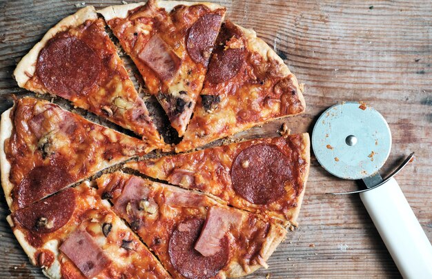 Okrągła pizza z salami i pastą pomidorową z okrągłym nożem na drewnianym tle Włoska kuchnia Domowa pizza