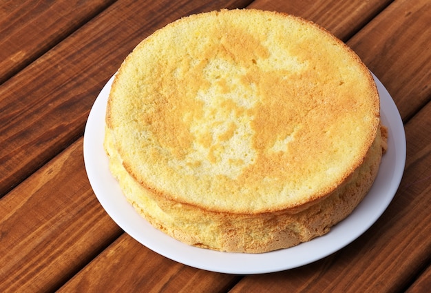 Okrągłe domowe ciastko biszkoptowe z mąki, cukru pudru, jajek na talerzu na drewnianym stole. Podstawa ciasta