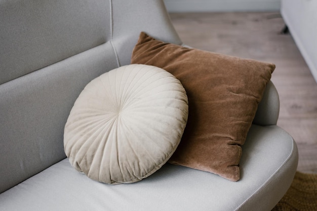 Okrągłe i kwadratowe przytulne poduszki na szarej kanapie w salonie z bliska