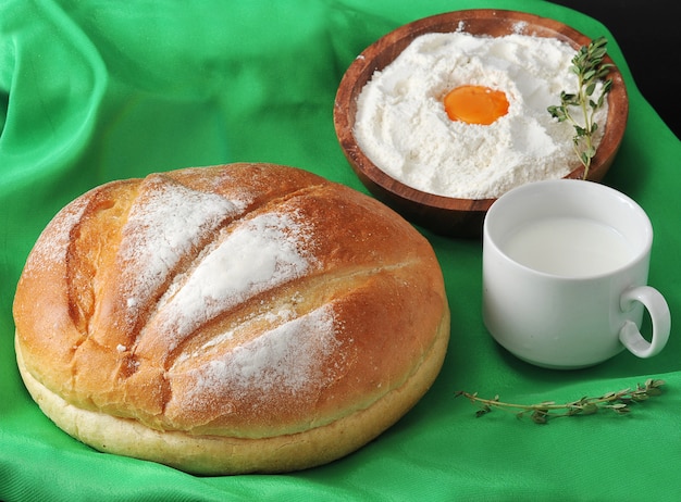 Okrągły bochenek chleba, mleko w filiżance i mąka z żółtkiem