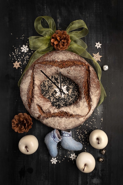Okrągły chleb żytni z suszonymi owocami na czarno. Świąteczne dekoracje, stylizacja zegara.