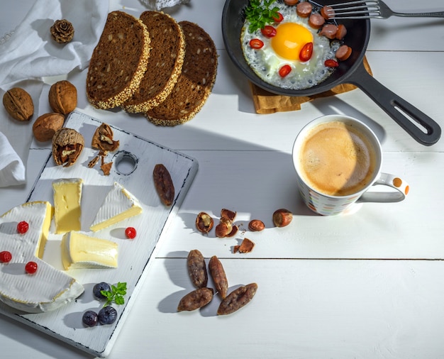 Okrągły ser Camembert na białej tablicy, jajka sadzone z kiełbasą i filiżanką kawy