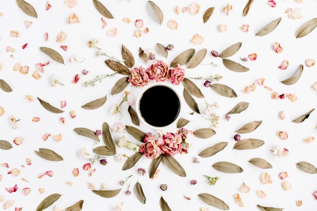 Zdjęcie okrągły wzór wieniec ramki z różami, filiżanką kawy, różowymi pąkami kwiatowymi, gałęziami i suszonymi liśćmi na białej powierzchni