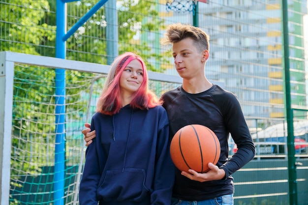 Okres dojrzewania, aktywny tryb życia w mieście, przyjaźń. Portret faceta i nastolatka przytulających się na boisku do koszykówki z piłką w dłoniach