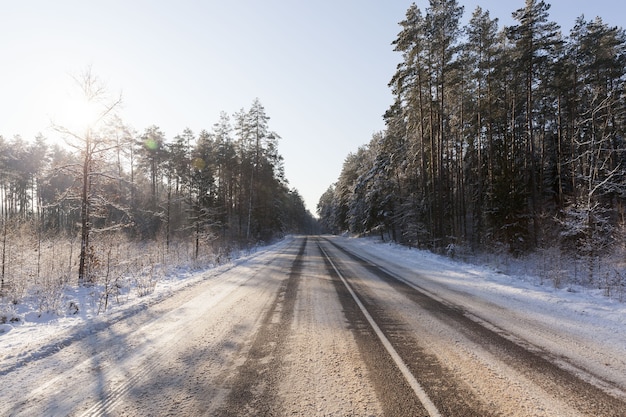 Okres zimowy na wąskiej drodze w lesie, droga pokryta śniegiem po opadach śniegu, mroźna pogoda na śliskiej i niebezpiecznej dla transportu drodze