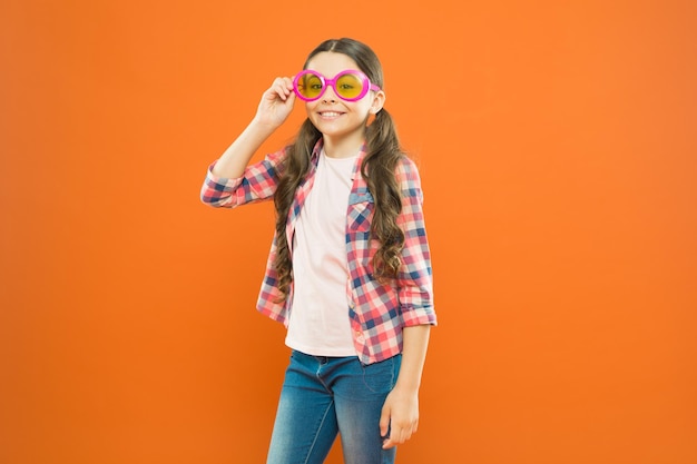 Okulary idealne do jej stylu Małe dziecko wyglądające na szczęśliwe w modnych okularach Małe dziecko uśmiechające się z imprezowymi okularami na pomarańczowym tle Zabawna dziewczyna nosi okulary przeciwsłoneczne z filtrem kolorów