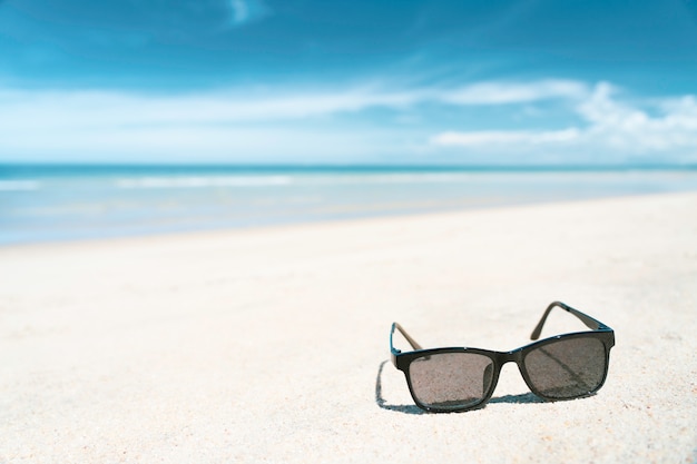 Okulary przeciwsłoneczne na białej piasek plaży z turkusowym koloru morzem w lato słonecznego dnia czasie