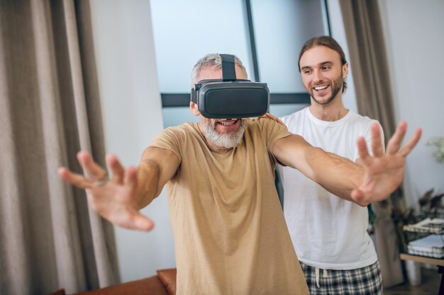 Okulary VR. Mężczyzna w okularach vr chodzący po pokoju, podtrzymujący go partner