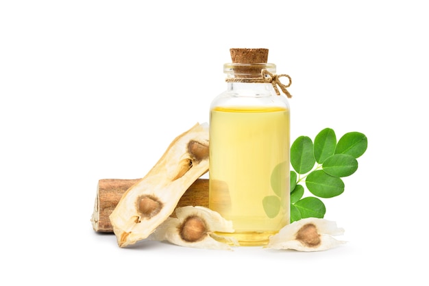 Olej moringa w szklanej butelce z suszonymi nasionami i zielonym liściem na białym tle.