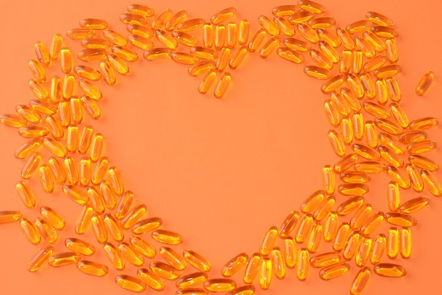 Olej rybny, Omega-3. Przydatne witaminy, leki w kapsułkach na pomarańczowym tle, w kształcie serca