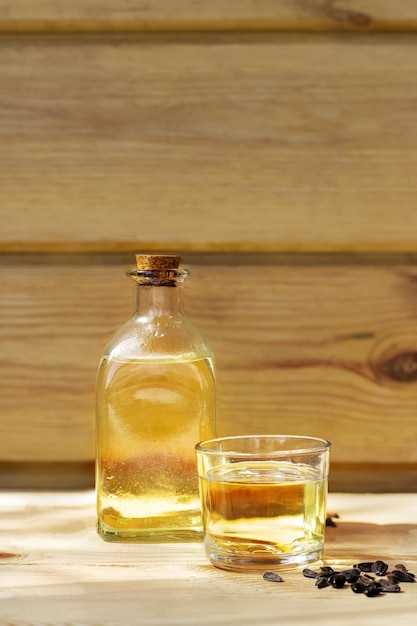 Olej słonecznikowy w szklanej butelce z nasionami na drewnianym tle