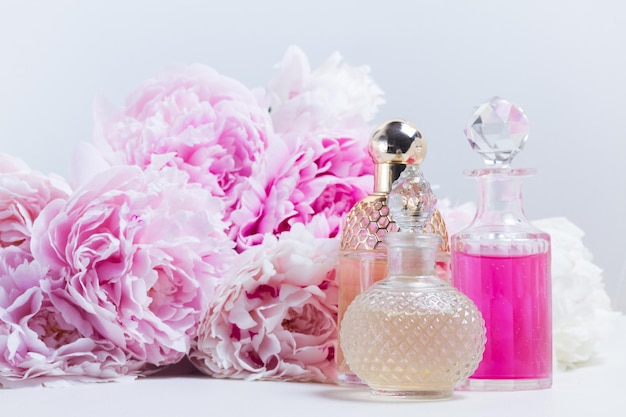 Zdjęcie olej z esencji piwonii różowej i woda w szklanych fiolkach oraz świeże kwiaty piwonii