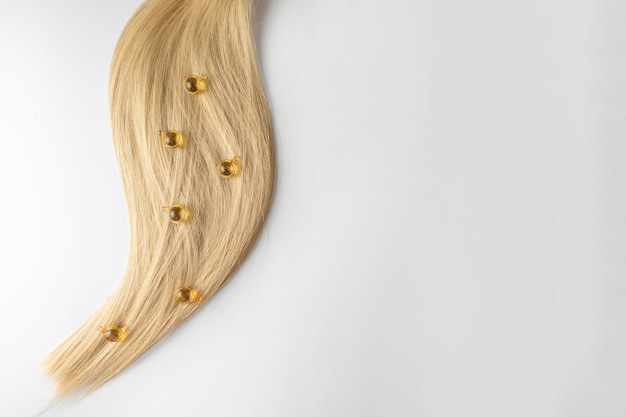 Olejek lub serum do pielęgnacji włosów w złotych kapsułkach leżące na kosmyku makiety marketingu produktów do włosów blond Koncepcja pielęgnacji włosów w salonie lub w domu