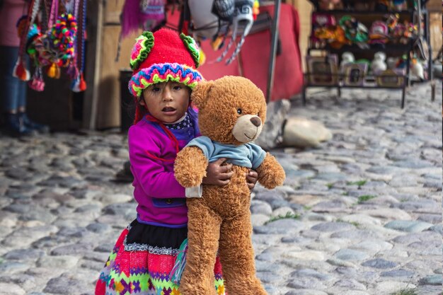 Ollantaytambo Peru 09102023 Peruwiańska dziewczynka w tradycyjnych ubraniach trzyma miękkiego miśka