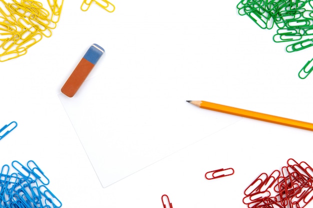 Ołówek, gumka, spinacze do papieru leżą pod różnymi kątami arkusza na białym tle. Obraz bohatera i miejsce na kopię.