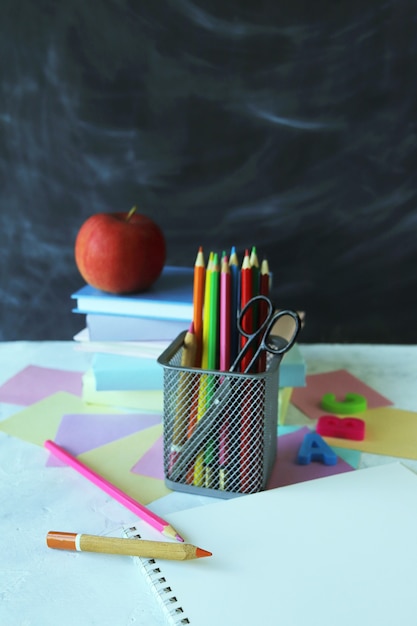 Ołówki wielobarwne litery stos książek i jabłko na tle tablicy szkolnej z powrotem do szkoły