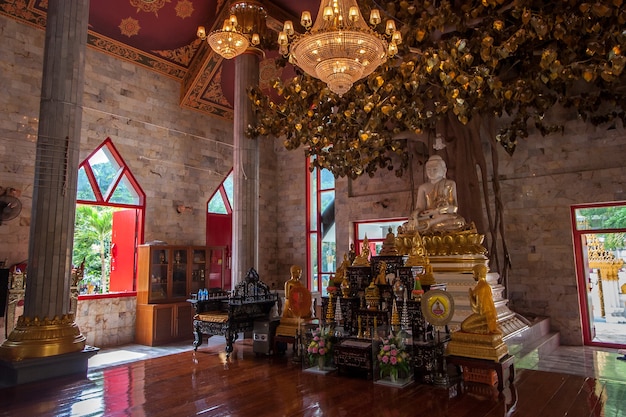 Ołtarz z posągiem Buddy i innymi dekoracjami w świątyni buddyjskiej. Drzewo życzeń i duże świecące żyrandole.