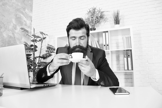 Omów biznes przy kawie Szanowany dyrektor generalny Mężczyzna przystojny szef siedzieć w biurze pijąc kawę Wygodne miejsce do pracy Dzień dobry Brodaty hipster formalny garnitur relaks przy kawie Procedury życia biurowego
