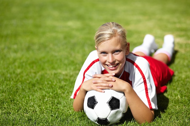 Ona jest kapitanem drużyny Portret atrakcyjnej futbolistki leżącej na trawie i opartej na piłce nożnej