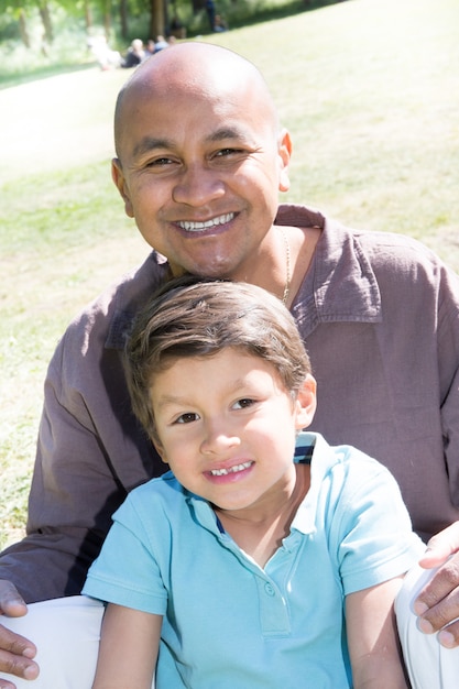 ondian lub meksykański mężczyzna siedzieć na trawie z mieszanym synem chłopiec dziecko na lato
